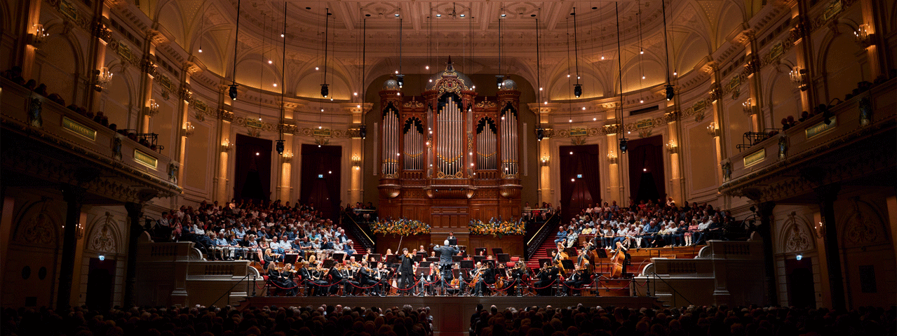 De Grote Zaal van het Koninklijk Concertgebouw van Amsterdam,waar een orkest speelt in de met publiek gevulde zaal voor het indrukwekkende orgel. Ontvang 50% korting op de VriendenLoterij ZomerConcerten met de VIP-KAART!