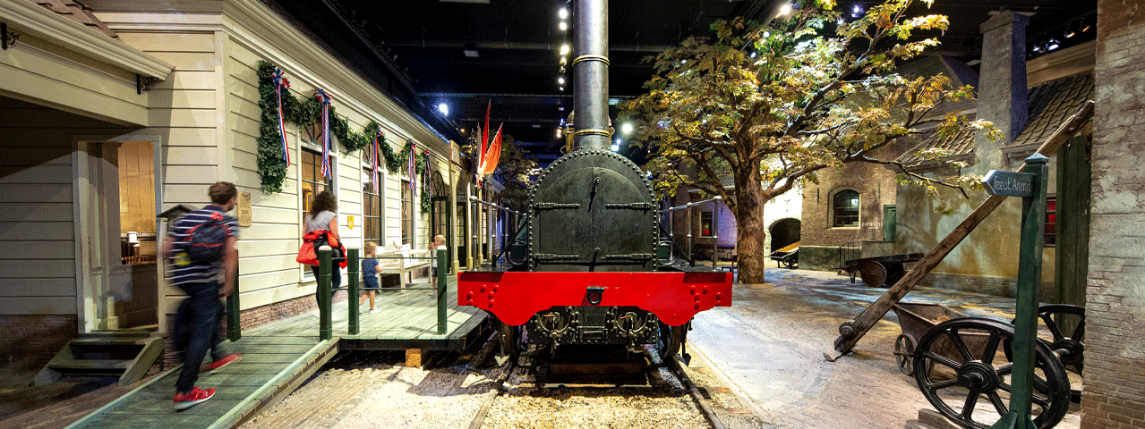 Interieur van het Spoorwegmuseum in Utrecht. In de donkere stationshal staat een historische stoomtrein, omringd door historische objecten en een oude wachtruimte. Deelnemers kunnen met de VIP-KAART gratis naar het Spoorwegmuseum.