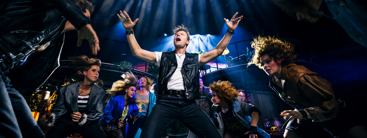 De cast van Doe Maar! de musical danst een rocknummer onder dramatische belichting. Ontvang korting op Doe Maar! De Nederpop musical met de VriendenLoterij VIP-KAART.