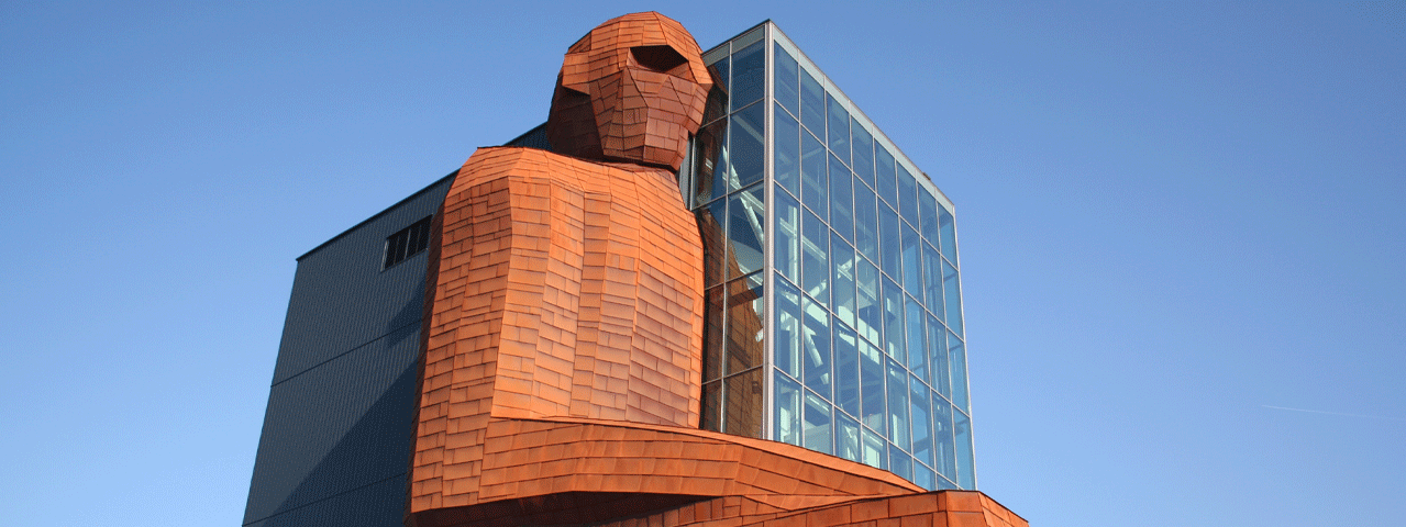 Het iconische CORPUS-gebouw in Oegstgeest, met de gigantische koperkleurige mensfiguur die half uit een modern glazen gebouw oprijst tegen een helderblauwe lucht. De opvallende combinatie van sculptuur en architectuur nodigt uit tot een ontdekkingsreis door het menselijk lichaam. Met de VIP-KAART krijg je korting op een bezoek aan CORPUS.