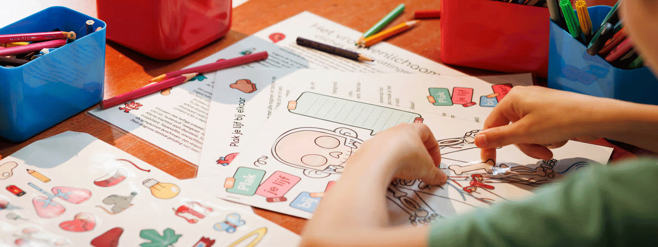 Een kind neemt deel aan een activiteit en plakt stickets op een tekening van een skelet. Om het kind heel liggen kleurrijke potloden.