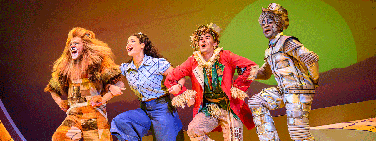 Vier acteurs, de leeuw, Dorothy, de vogelverschrikker en de blikken man dansen arm in arm in de vrolijke productie the WIZ. Ontdek de musical The WIZ met 50% korting met de VIP-KAART.
