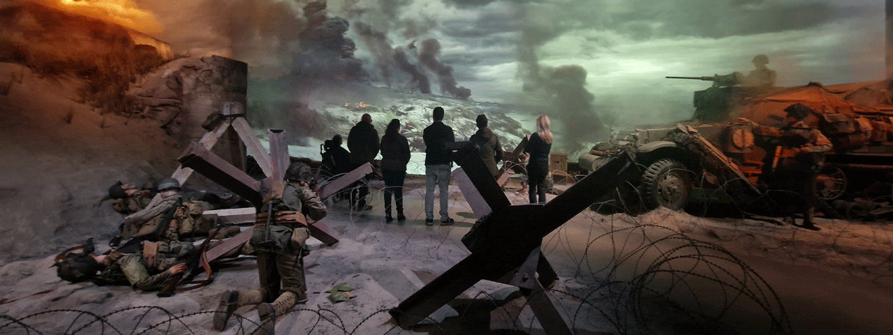 Bezoekers staan in een geënsceneerd oorlogsdecor met tanks. Op de achtergrond doemen rookpluimen op. Met de VIP-KAART bezoekt u Oorlogsmuseum Overloon gratis.