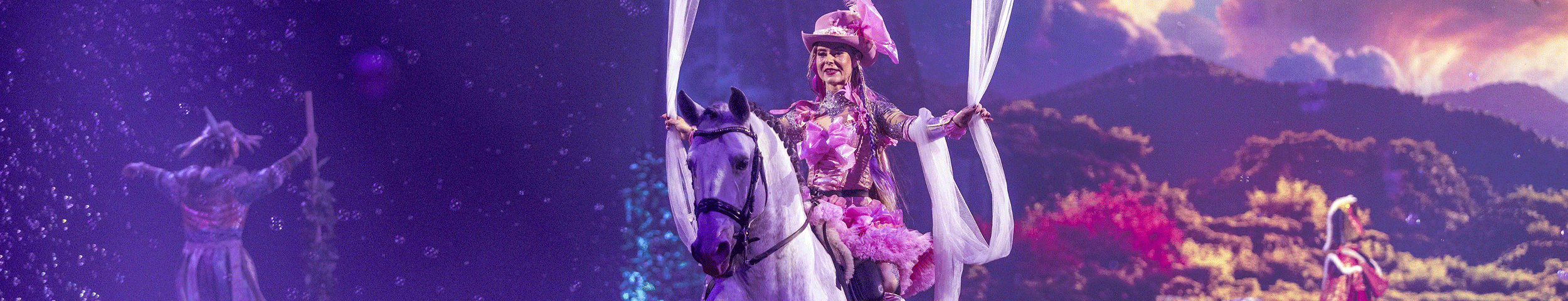 Een vrouw in roze kostuum rijdt op een wit paard tijdens paardenshow Cavalluna. Ontvang 50% korting op tickets voor paardenshow Cavalluna met de VriendenLoterij VIP-KAART.