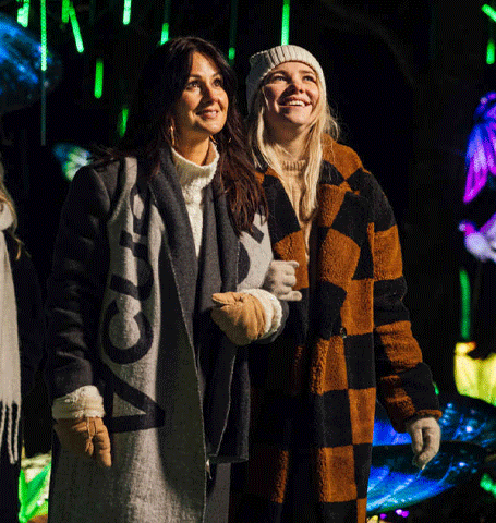 Vier vriendinnen in winterkleding lopen door een kleurrijke wereld vol lichtgevende kunstwerken.