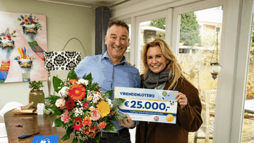 Een man en vrouw staan in een woonkamer met een bos bloemen en tonen een cheque van €25.000 van de VriendenLoterij.