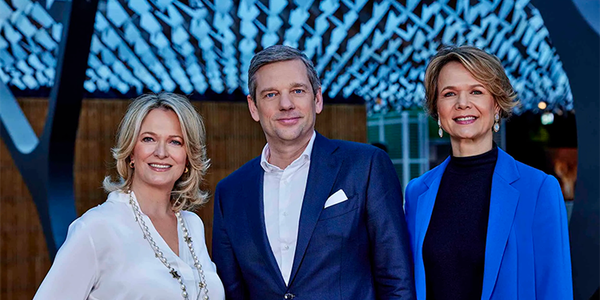 Imme Rog, Michiel Verboven en Sigrid van Aken Raad van Bestuur van de Postcode Lottery Group staan onder het iconische dak van de Beethovenstraat 200. Ze kijken in de camera en dragen zakelijke kleding.