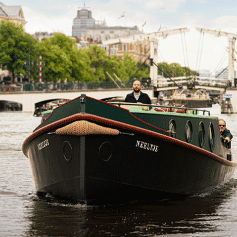 Een boot vaart op de Amstel, met op de achtergrond de Magere Brug en zicht op Amsterdam. Met de VIP-KAART vaart u voordelig mee met de Cultuur Ferry door Amsterdam.
