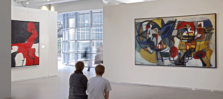 Twee bezoekers kijken naar de kleurrijke schilderijen in de lichte museumzaal van Museum Cobra. Deelnemers bezoeken dit museum gratis met de VIP-KAART