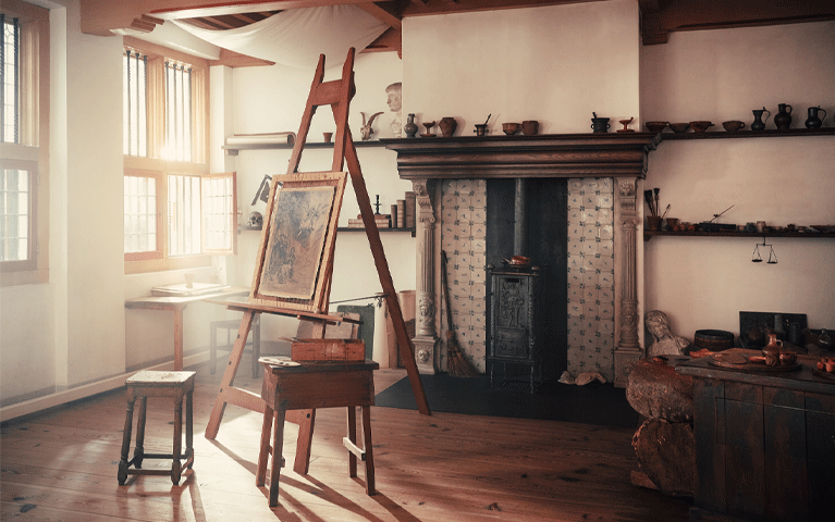 Zacht zonlicht schijnt op een historisch atelier met een ezel en een openhaard met authentieke tegeltjes. Bezoek Museum Rembrandthuis met de VIP-KAART met gratis entree.