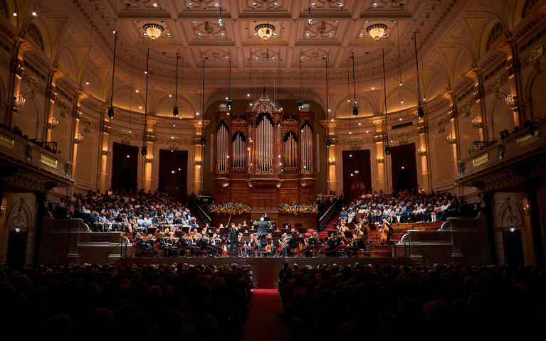 De Grote Zaal van het Koninklijk Concertgebouw van Amsterdam,waar een orkest speelt in de met publiek gevulde zaal voor het indrukwekkende orgel. Ontvang 50% korting op de VriendenLoterij ZomerConcerten met de VIP-KAART!