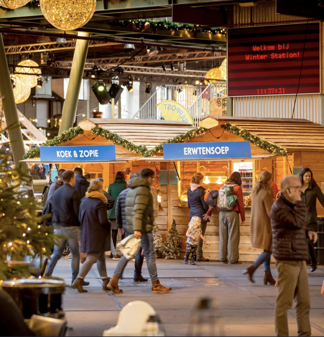 Mensen lopen door een winterse setting in het Spoorwegmuseum en kijken bij de kraampjes met Erwtensoep en Koek & Zopie. In de winter kunt u gratis naar Winterstation met de VIP-KAART.