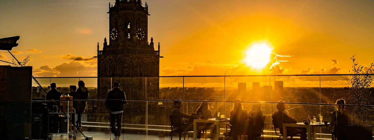 Mensen genieten van de ondergaande zon op het dakterras bij Forum Groningen, met uitzicht over de stad en de Martinitoren. Met de VIP-KAART bezoekt u Forum Groningen gratis.
