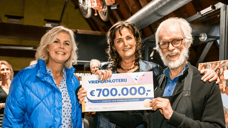 Drie mensen poseren met een cheque van €700.000 van de VriendenLoterij voor het Marius van Dokkum Museum.