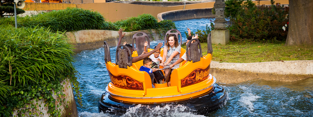 Een vrouw en kinderen zitten lachend in een gele boot op een wildwaterbaan vol klotsend water