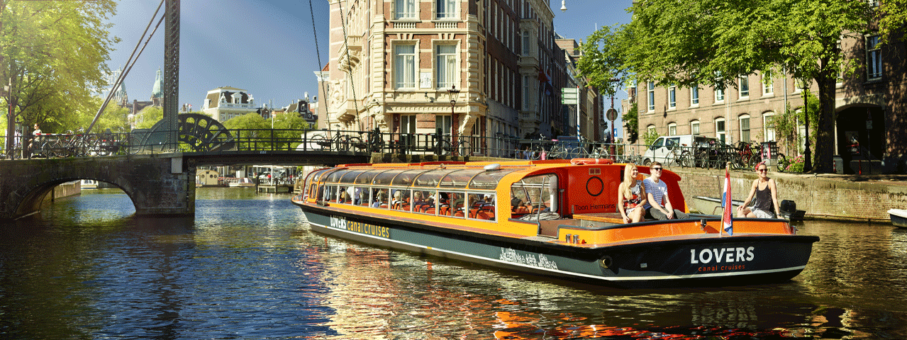 Een boot van rederij Lovers vaart over de Amsterdamse grachten op een zonnige dag