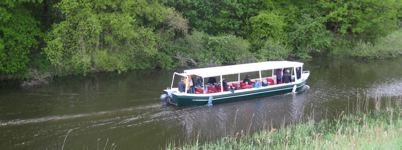 Een rondvaartboot vaart door een groen natuurgebied.