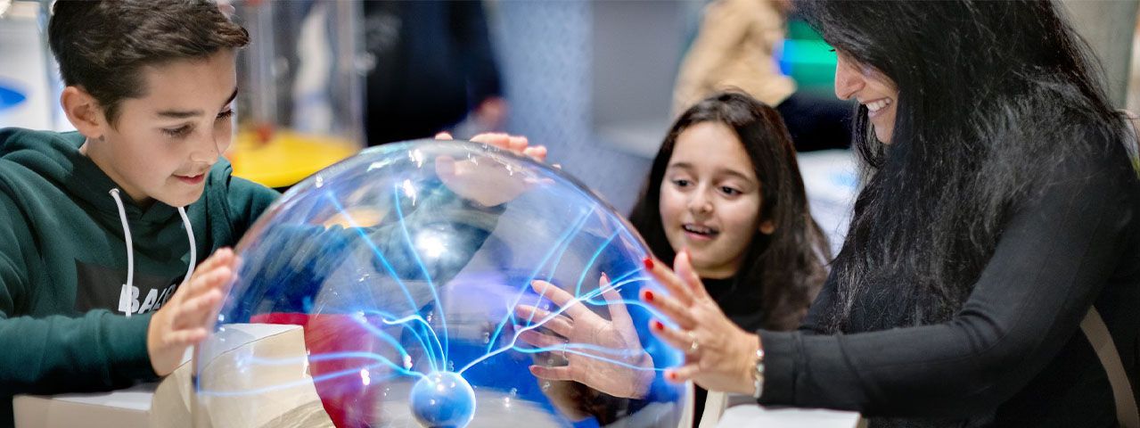 Een vrouw en twee kinderen leggen hun handen op een bliksembol in wetenschapsmuseum NEMO