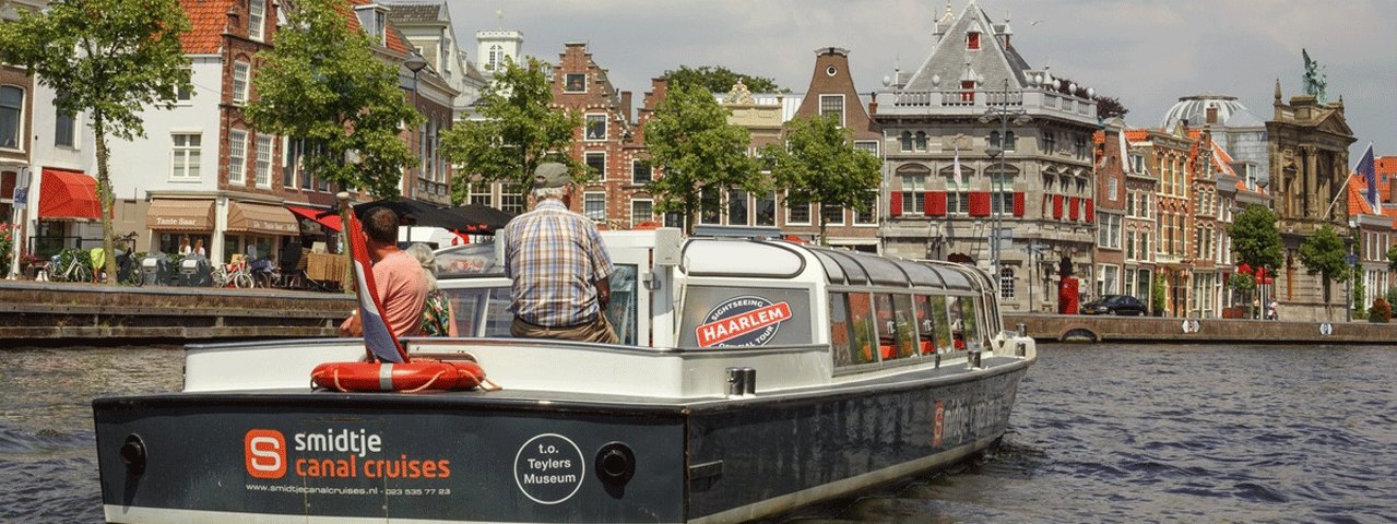 Een rondvaartboot vaart over de gracht langs de historische huizen van Haarlem