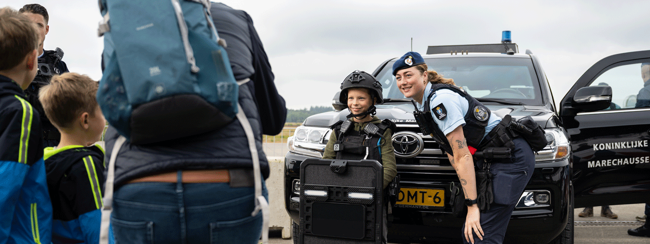 Een officier van de Koninklijke Marechaussee poseert voor haar auto met een kind voor een foto.