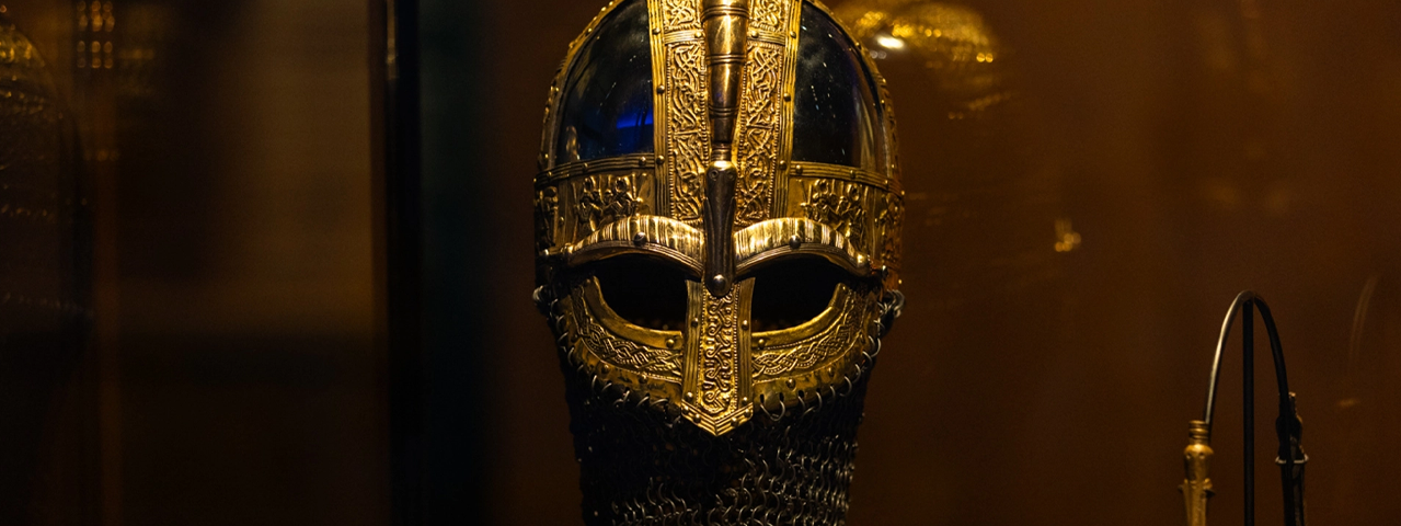 Een middeleeuwse helm voor een krijger versierd met abstracte decoraties in een museumvitrine.