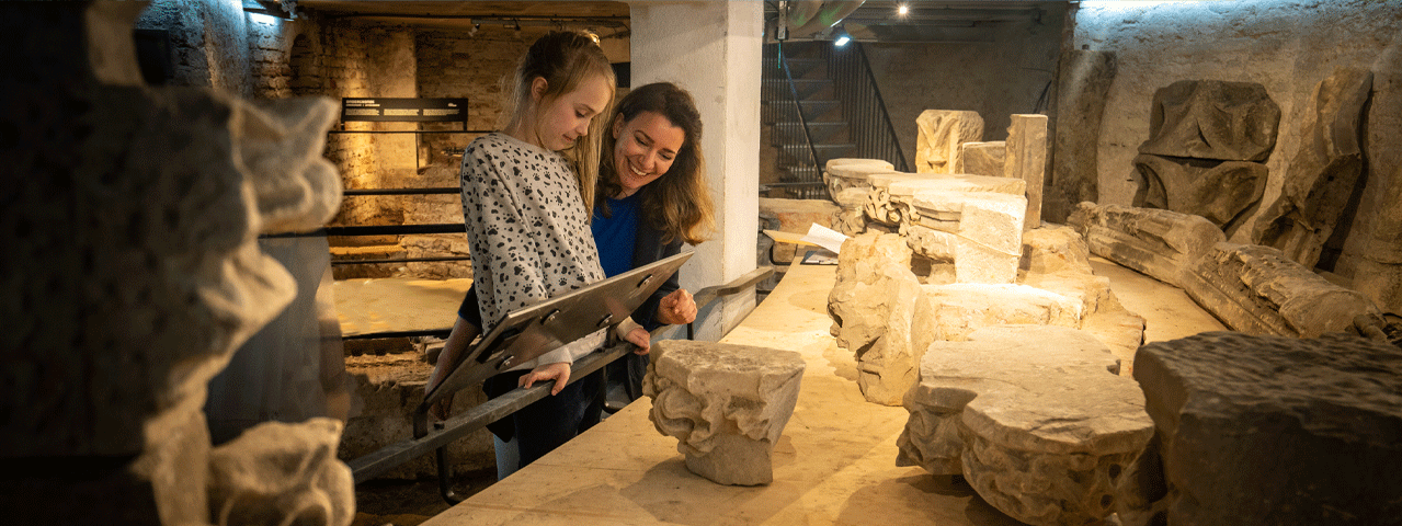 Een vrouw en een kind bekijken samen oude overblijfselen van stenen pilaren in de Eusebiuskerk. Bezoek deze kerk gratis met de VIP-KAART