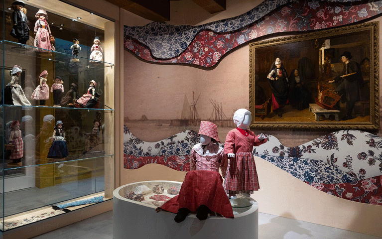Een zaal in Museum Hindeloopen over de Hindelooper klederdracht. In de ruimte staan poppen in diverse klederdracht, met op de achtergrond een traditioneel patroon. Met de VIP-KAART is dit museum gratis te bezoeken.