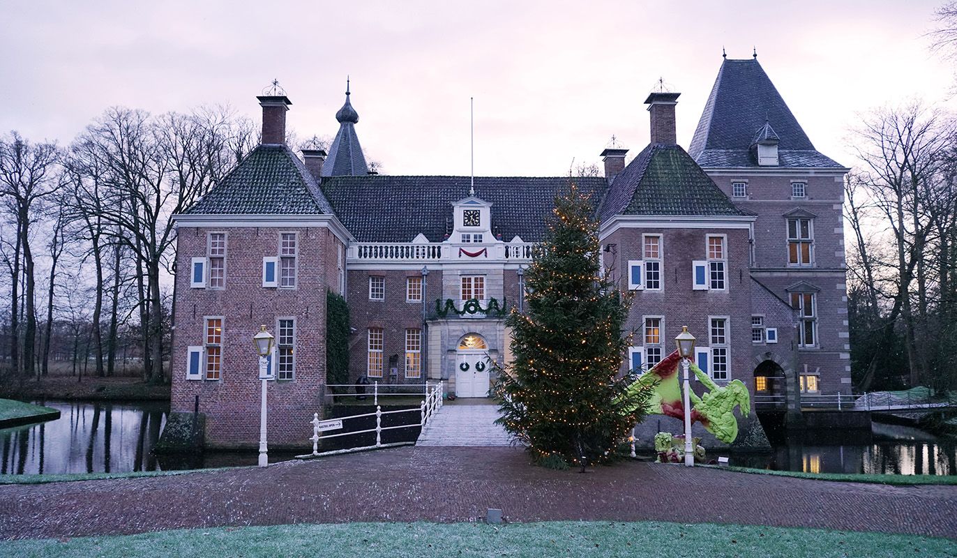 Winterse aanblik van Kasteel Het Nijenhuis bij Zwolle, met feestelijke kerstversiering, een verlichte boom en kunstwerken in de tuin. Gratis te bezoeken met de VriendenLoterij VIP-KAART.