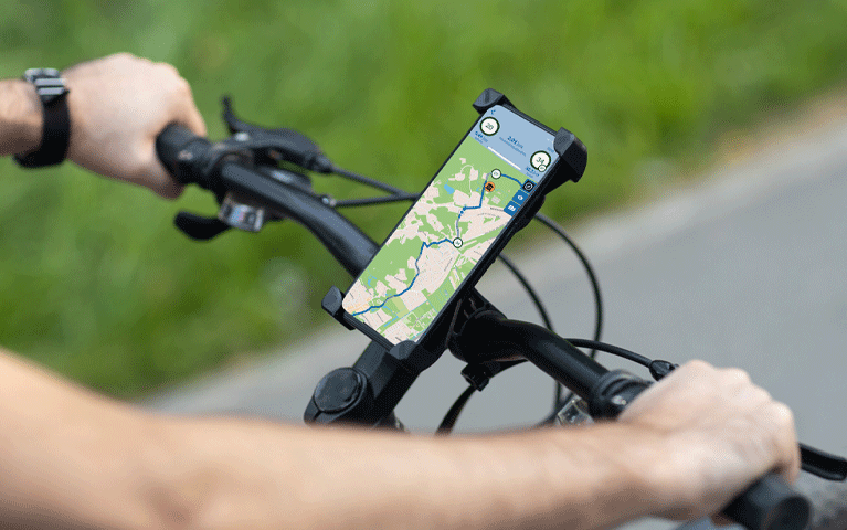 Een close-up foto van twee armen leunend op een fietsstuur. Op het fietsstuur is een mobiele telefoon bevestigd met daarop een app die een fietsroute laat zien. Fietsnetwerk Premium is Gratis met de VIP-KAART