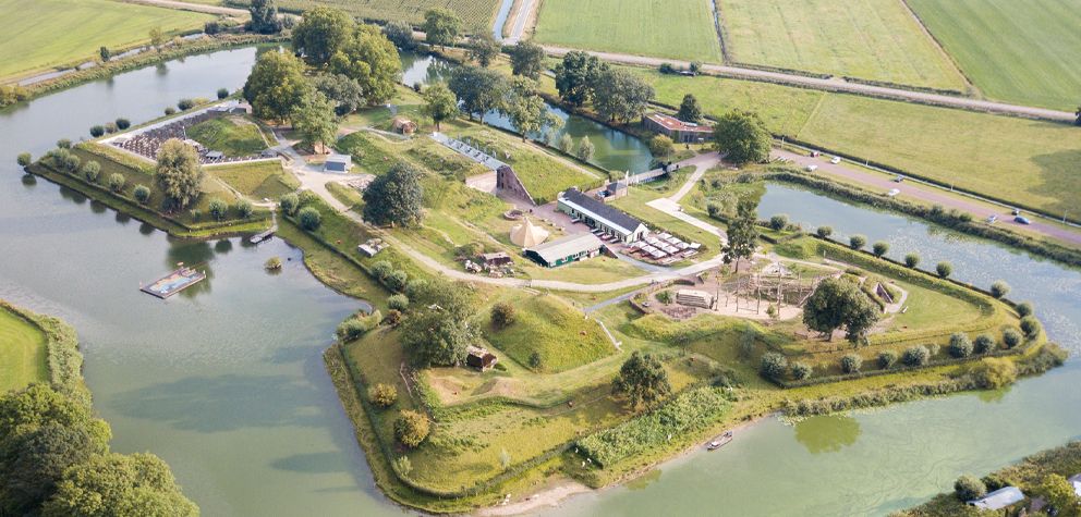 Het stervormige forteiland Geofort gezien vanuit de lucht. Het forteiland is erg groen door het gras en verspreid staan diverse gebouwen waar leuke activiteiten worden gehouden.