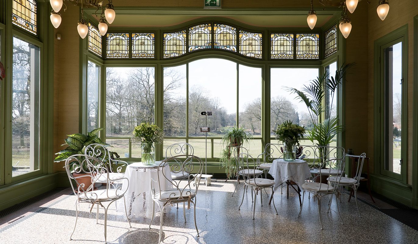 Elegante serre van Museumhuis Rams Woerthe in Steenwijk, met gietijzeren stoelen, tafels met kanten kleedjes en uitzicht op het omliggende park. Gratis te bezoeken met de VriendenLoterij VIP-KAART.