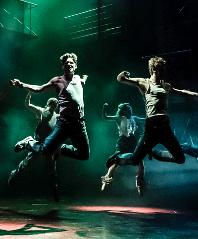 Twee dansers springen energiek in de lucht op het podium. Ontdek musicals met korting met de VriendenLoterij VIP-KAART