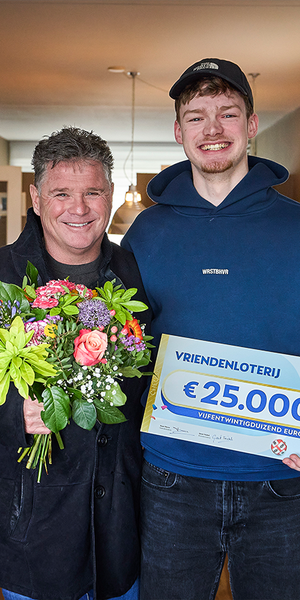 Een jongeman poseert met een cheque van €25.000 van de VriendenLoterij naast Wolter Kroes met een bos bloemen.
