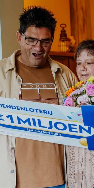 Man bekijkt samen met zijn partner verrast een cheque van €1 miljoen van de VriendenLoterij.