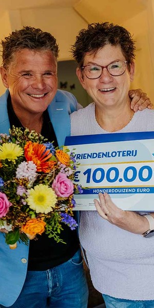 Mevrouw poseert met een cheque van €100.000 van de VriendenLoterij en een bos bloemen.