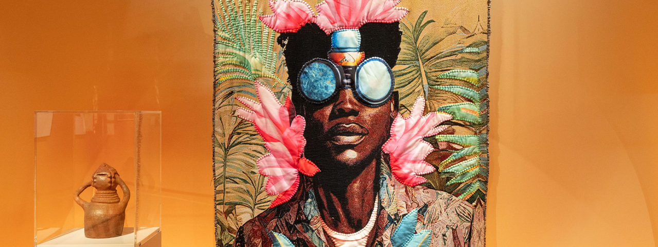 Een kleurrijk kunstwerk hangt voor een oranje muur in Wereldmuseum Rotterdam. Bezoek het Wereldmuseum Rotterdam gratis met de VIP-KAART.