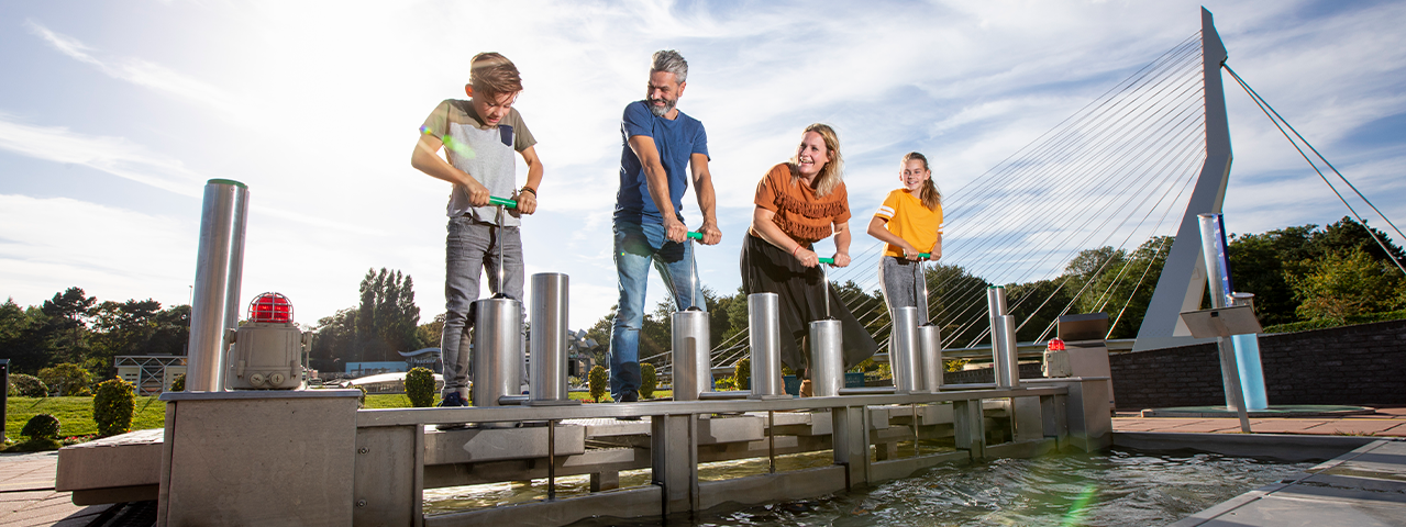 Een familie neemt deel aan een leuke activiteit in Madurodam en probeert gezamenlijk een sluis vol water dicht te krijgen. Met de VIP-KAART is een bezoek aan Madurodam gratis.