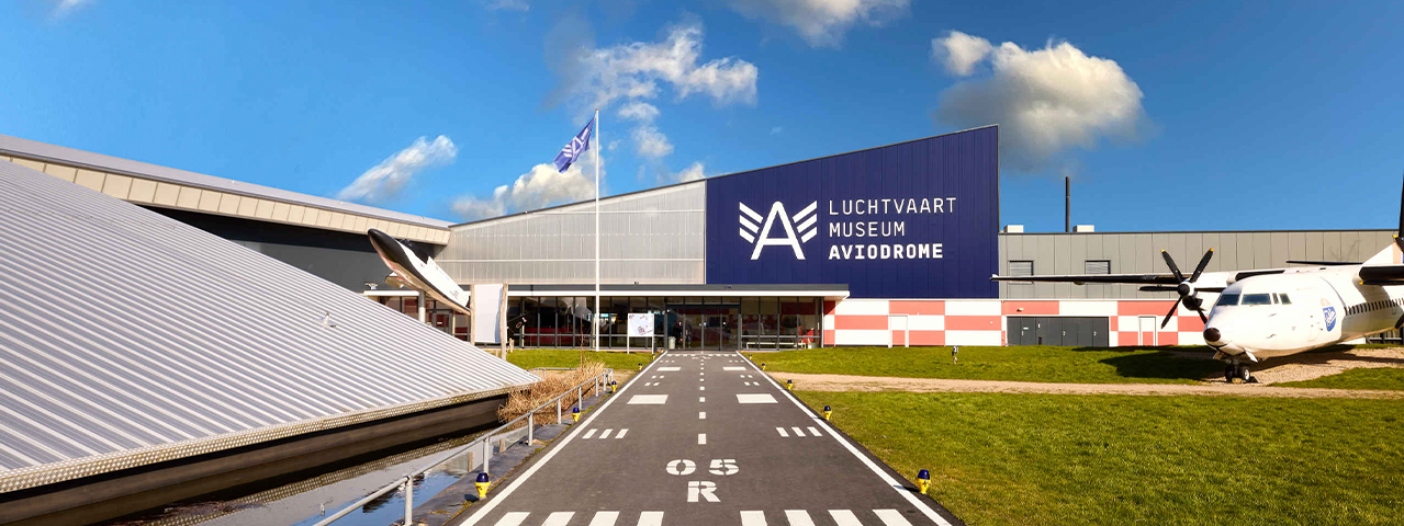 Entree van Luchtvaartmuseum Aviodrome, met een nagebouwde landingsbaan en een vliegtuig op het grasveld. Deelnemers kunnen met hun VIP-KAART dit museum gratis bezoeken en ontdekken alles over de geschiedenis van de luchtvaart.