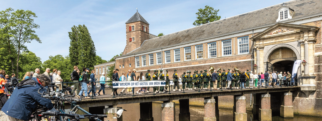 Een rij mensen beloopt de loopbrug van Kasteel Breda, een historisch slot met imposante uitstraling.