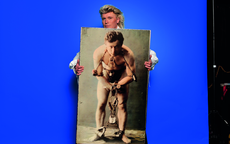 Een man houdt een grote foto vast van de bekende goochelaar Houdini in boeien voor een blauwe achtergrond