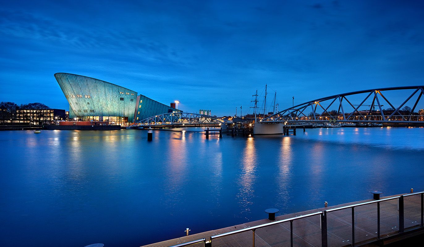 Zicht over het water op het NEMO Science Museum in de avond. Met de VIP-KAART krijgt u een gratis entreeticket voor dit wetenschapsmuseum.