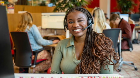 Een blije medewerker van Ledenservice met een headset op haar hoofd.