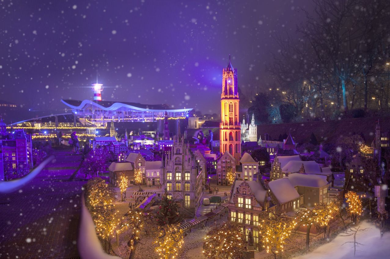 Een zicht op de miniatuurwereld van Madurodam in de avond, sfeervol verlicht terwijl er sneeuwvlokken door het beeld dwarrelen. Met de VIP-KAART bezoekt u Madurodam helemaal gratis!