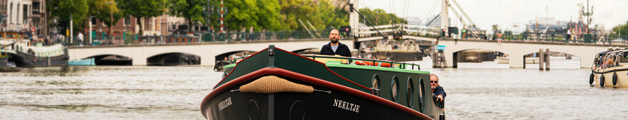 Een boot vaart op de Amstel, met op de achtergrond de Magere Brug en zicht op Amsterdam. Met de VIP-KAART vaart u voordelig mee met de Cultuur Ferry door Amsterdam.