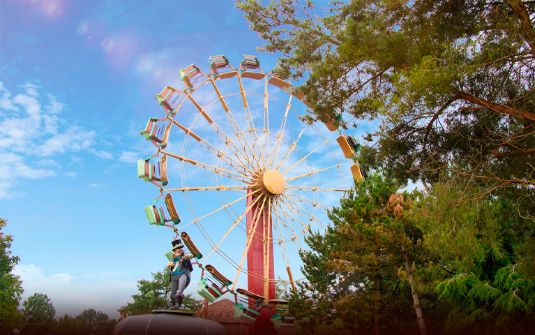 Een groot reuzenrad voor een stralende lucht in een groene omgeving bij Attractiepark Slagharen.